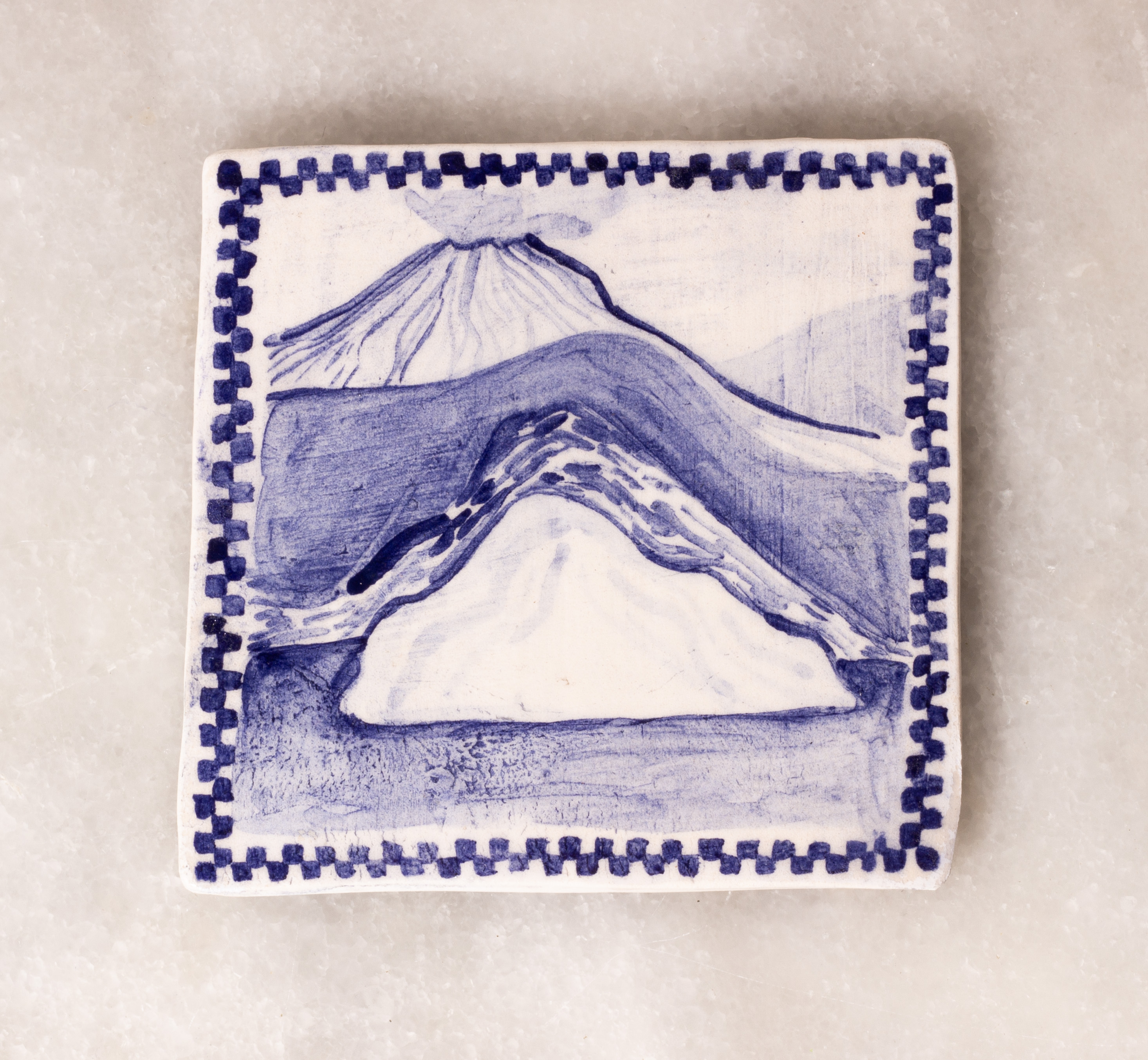 carreau de faïence blanc peint en bleu à l'oxyde de cobalt. Il représente plusieurs volcans en enfilade, celui du fond fume