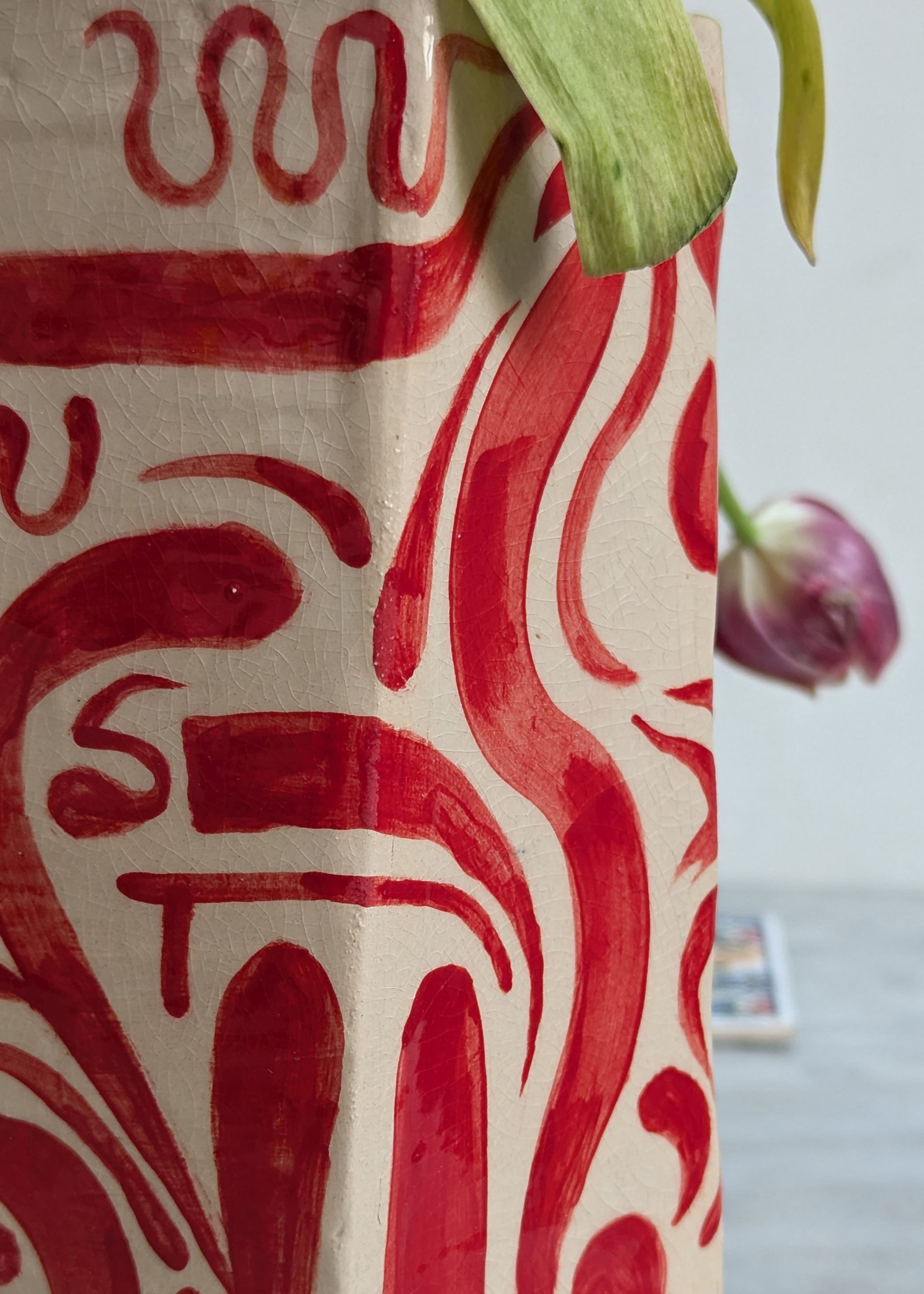 détail de vase en faïence blanche peinte avec des motifs abstraits rouges, dans lequel on voit un bouquet de tulipes rouges et jaunes, posé sur une table en marbre